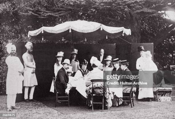 Queen Victoria holds a garden party with members of her family in the grounds of Osborne House on the Isle of Wight. Two Indian servants wearing...