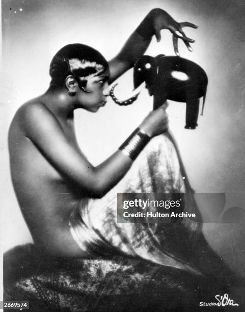 American dancer and singer Josephine Baker poses with a model of an elephant.