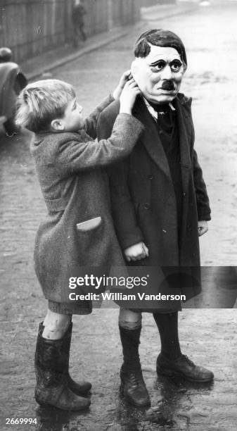 Young boy adjusts his friend's Adolf Hitler mask during a game on a street in King's Cross, London.