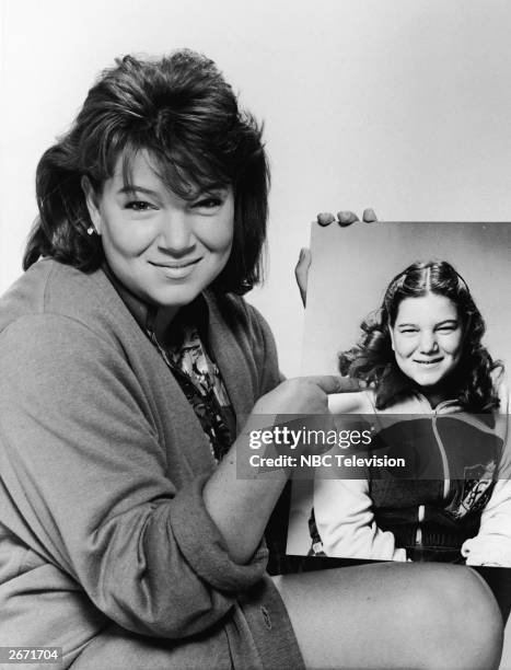 Promotional portrait of American actor Mindy Cohn pointing to a publicity picture of herself from 1979, the year the television series 'The Facts Of...