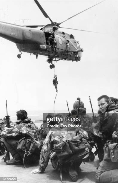 Waiting to be lifted by a Westland Sea King helicopter, Royal Marines from 40 Commando crouch on the flight deck of HMS Hermes, which heads the naval...