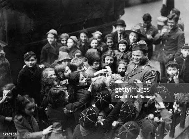 Soldier enjoys giving out his candy ration to a group of children in the East End of London on Thanksgiving Day.One boy, behind the soldier, is not...