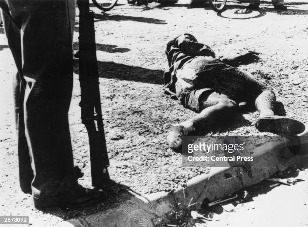 An armed man stands beside the body of one of the sixty-nine black South Africans killed by police in the massacre at Sharpeville, South Africa,...