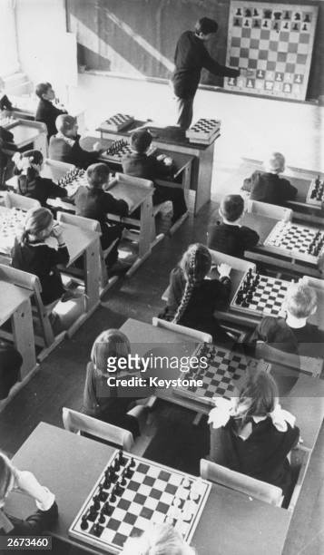 Young pupils at a school in Pskov, Russia, each with a chess board on their desk, watch as their teacher uses a giant chess board to teach a chess...
