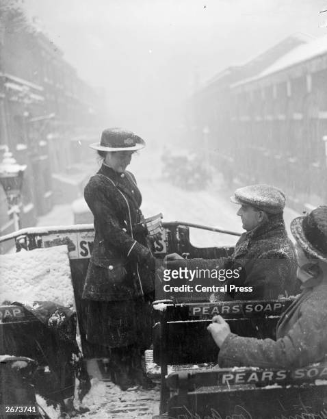 Bus conductress at work on the top deck of an open-top bus in the snow during World War I.