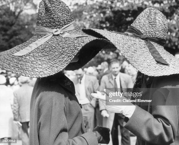 Two women wearing large, floppy brimmed, straw hats have a chat during a visit to the Chelsea Flower Show. The one on the left is navy the one on the...