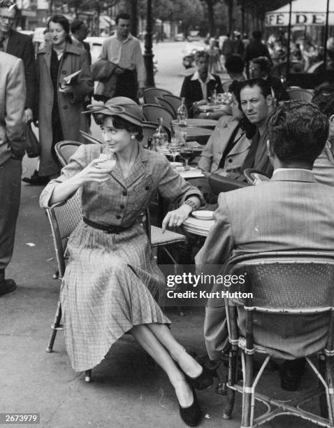 Chic Parisienne sips an aperitif outside a cafe in Paris. She is wearing a low-priced, mass-produced yet fashionable British dress designed by Norman...