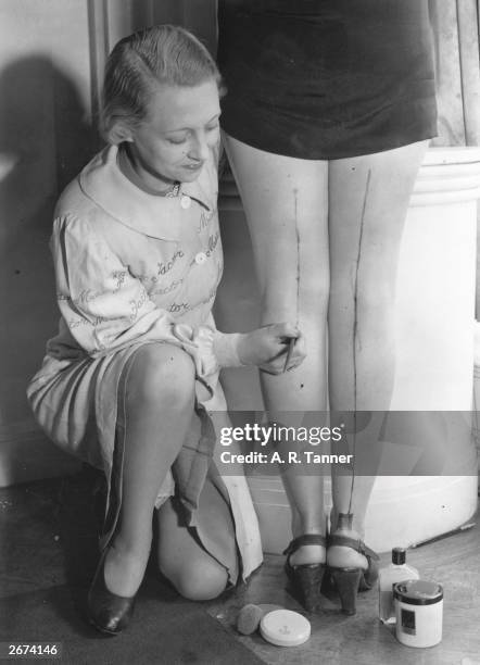 Max Factor beautician paints a seam on a woman's leg to help create the illusion of stockings during a WWII shortage, UK, 23rd May 1940.