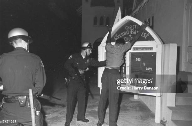 Suspect being searched by two armed police during the Watts riots in Los Angeles, California, 11th-15th August 1965.