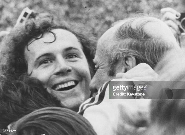 West German footballer Franz Beckenbauer beams with joy as he is embraced by coach Helmut Schon, after his team beat Holland 2-1 to win the 1974...