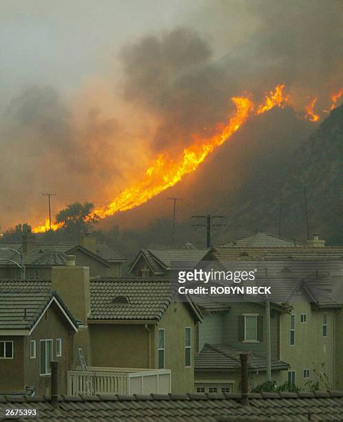 Flames crest a hill threatening homes in the Stevenson Ranch section of Santa Clarita in Los Angeles Country, 28 October 2003, as wildfires continue...