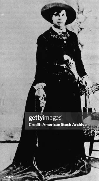 Full-length portrait of American outlaw Belle Starr , in a floor-length dress with a gun in one hand and the other resting on the back of a chair,...