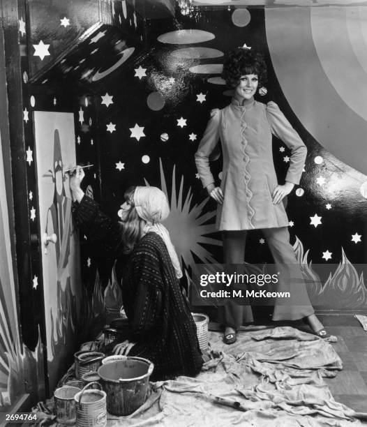 Paulene Stone models a velvet coat, price 16 guineas, from Apple Boutique, while at her feet a young woman surrounded by tins of paint and dust...