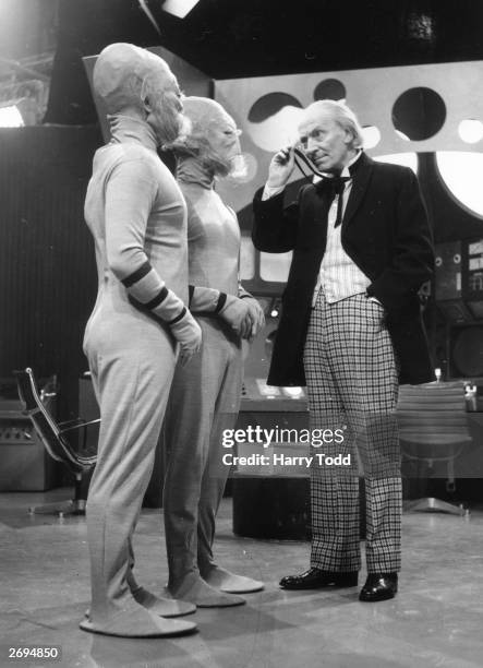 William Hartnell as Dr Who, peers through his monocle at two extra-terrestrials during filming of the popular science fiction series, 'Dr Who' at the...