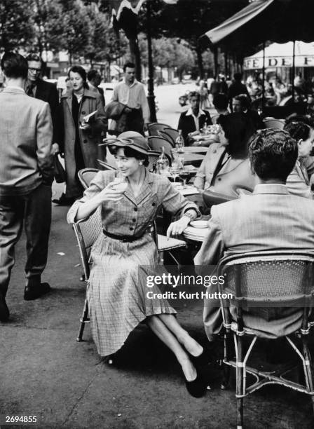 Parisian woman wearing a British dress of pleated grey-green check, drinks an aperitif in a cafe in St Germain des Pres. Original Publication:...