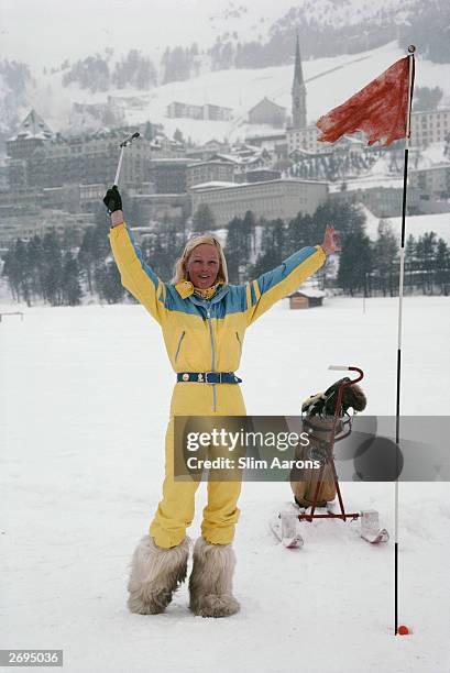 Wearing a yellow ski-suit and yeti boots and with a golf trolley on skis, Didi Fenton on 'the green' of a snow covered golf course at St Moritz.