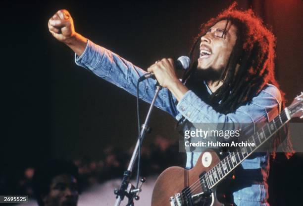 Jamaican Reggae musician, songwriter, and singer Bob Marley performs on stage, in a concert at Grona Lund, Stockholm, Sweden. He extends his fist as...