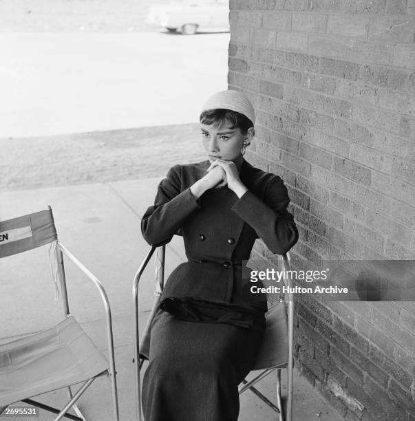 Belgian-born actor Audrey Hepburn , wearing a costume designed by Hubert de Givenchy, sits in a folding chair between takes on the set of director...
