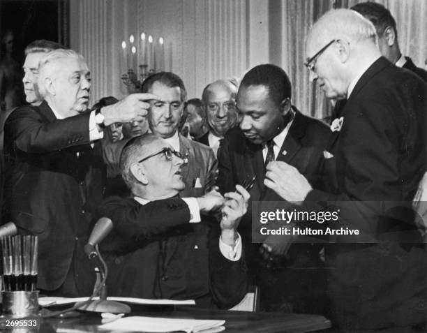 President Lyndon B Johnson shakes the hand of Dr Martin Luther King Jr at the signing of the Civil Rights Act while officials look on, Washington DC.