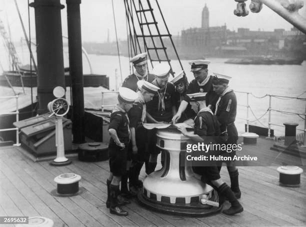 Full-length image of naval officers showing boys from the English Sea Scouts a chart at a capstan aboard a ship in the Thames River, London, England,...