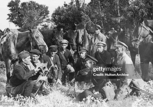 Group of Cossack fighters crouch in a field while a soldier demonstrates the use of a gas mask during the Russian Civil War that followed the...