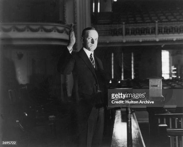 President Calvin Coolidge raises his right hand while standing at a podium for his swearing-in ceremony, Washington, D.C. He served two terms.