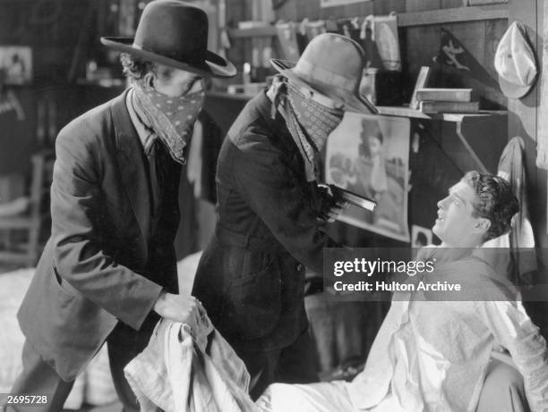 Two masked bandits use a gun to hold up a man, possibly American actor Cullen Landis, while he sits in bed in his pajamas in an unidentified film...