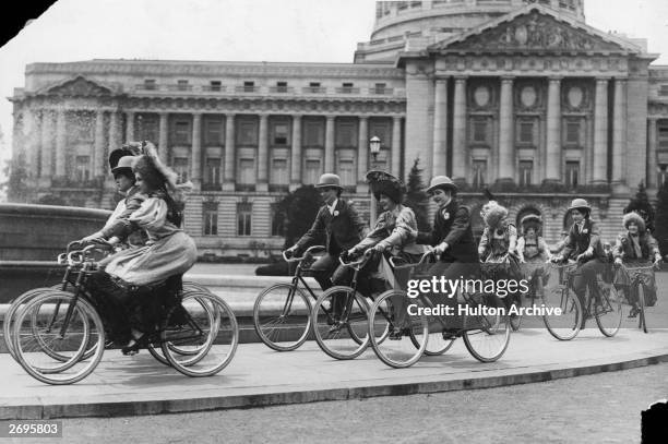 Society ladies ride bicycles around the fountain at City Hall while reenacting an old-style bicycle race in San Francisco, California. Several of the...