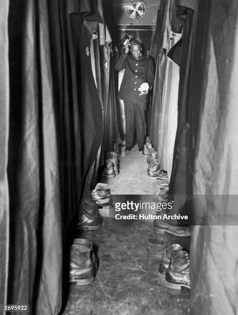 Pullman porter at the end of a train car corridor scratches his head and holds show polish and cloths as he contemplates the pairs of shoes arrayed...