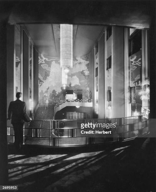 Man, seen from behind, leans against the railing of the gallery in the lobby of Radio City Music Hall in New York City. An Art Deco fresco decorates...