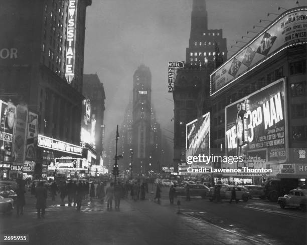 View of pedestrians and cars moving between theaters, storefronts, and hotels lit up with neon signs at night along Broadway in Times Square, New...