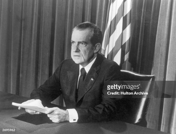 President Richard M. Nixon sits at a desk, holding papers, as he announces his resignation on television, Washington, D.C.