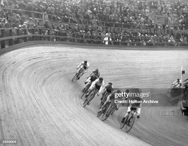 Group of bicyclists travel in a pack while taking a turn on a slanted track during a race at the Velodrome in New York City, 1930s. Spectators watch...