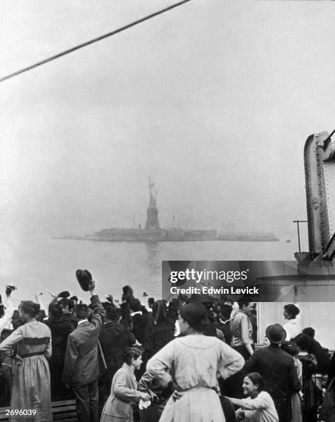 Group of immigrants traveling aboard a ship celebrate as they catch their first glimpse of the Statue of Liberty and Ellis Island in New York Harbor.