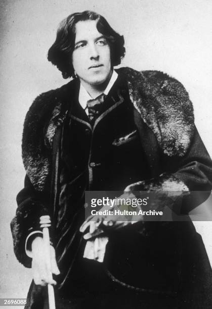 Portrait of Irish-born author and critic Oscar Wilde wearing a fur stole and holding a cane and gloves. Photograph taken by Napoleon Sarony.