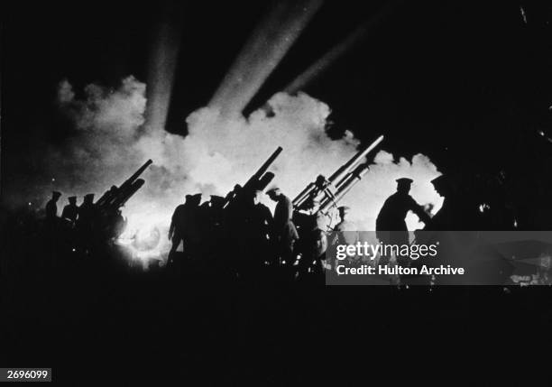 Silhouette of American soldiers manning 3-inch antiaircraft gun batteries as spotlights search the night skies for incoming planes during World War I.