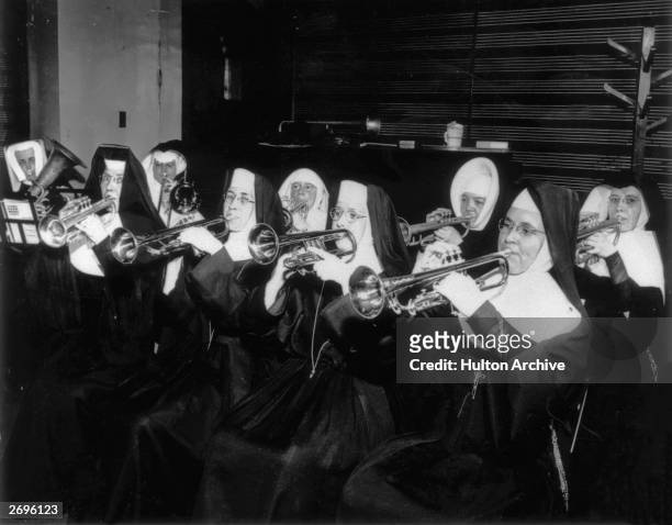 Brass section comprised of nuns, including one tuba, one trombone, and seven trumpets, playing their instruments. They all wear habits.