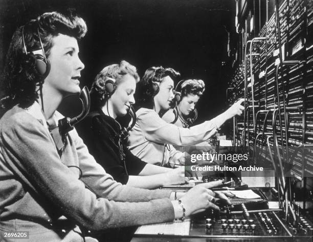 Four operators connect calls while working at a switchboard.