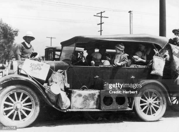 Car full of 'Oakies,' refugees from the Dust Bowl, look for work in San Francisco, California. Some of their possessions are secured to the running...