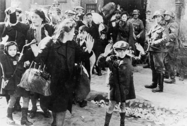 Group of Jewish civilians being held at gunpoint by German SS troops after being forced out of a bunker where they were sheltering during the Warsaw...
