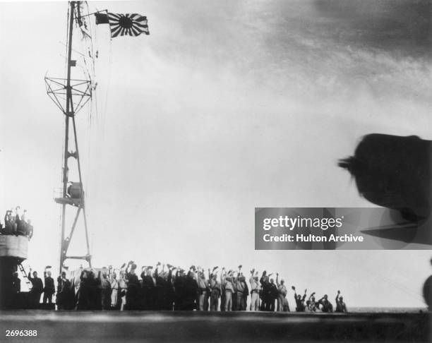 Japanese soldiers on an aircraft carrier wave at a plane from under their flag just before the attack on Pearl Harbor, Hawaii, World War II.