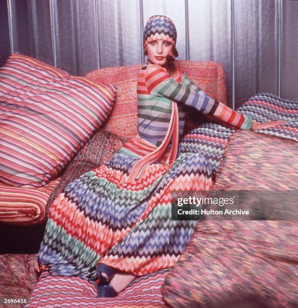 Portrait of a model wearing a colorful outfit designed by Missoni while posing on pillows covered in Missoni fabric. The outfit consists of a...