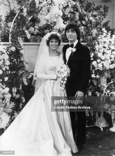 American actors Erin Moran, wearing a wedding dress, and Scott Baio, wearing a tuxedo, pose at an altar in a promotional portrait from the TV program...