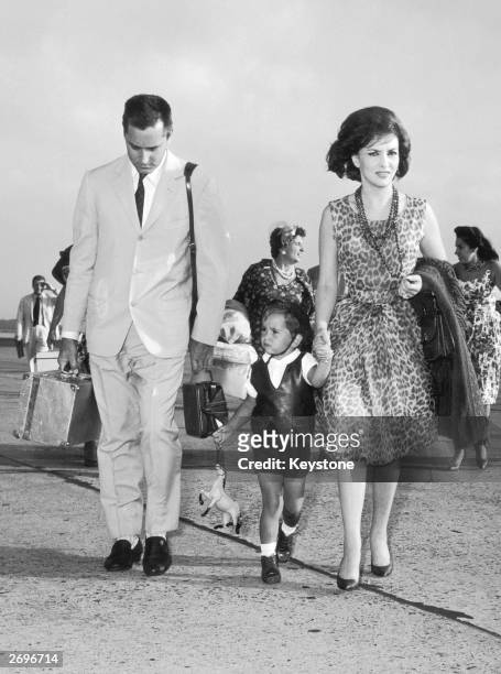 Wearing a sleeveless leopard-print dress and a triple strand of long beads, film star Gina Lollobrigida. She is at Rome airport with her husband...