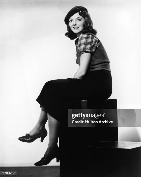 Full-length portrait of American actor Janet Gaynor wearing a beret and sweater vest and sitting on a cube, circa 1940.