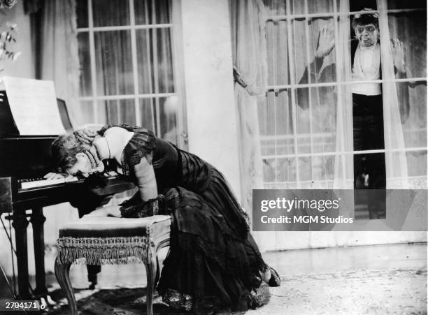 American actor Fredric March , in make-up as the monster Mr. Hyde, looks though a window at actor Rose Hobart who is slumped over a piano in a still...