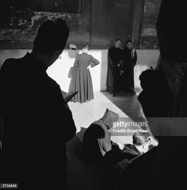 Silhouette of a priest in a biretta and a monk in a cowl are among a group of priests gathered on steps somewhere in Rome. Original Publication: In...