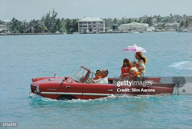 Film producer Kevin McClory takes his wife Bobo Sigrist and their family for a drive in an 'Amphicar' across the harbour at Nassau, 1967. The...