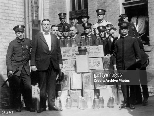 Group portrait of a police department liquor squad posing outdoors with cases of confiscated alcohol and distilling equipment during Prohibition.