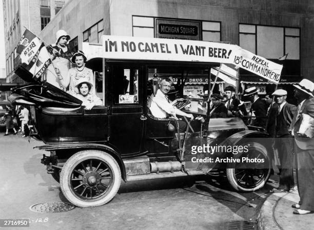 Prohibition protesters parade in a car emblazoned with signs and flags calling for the repeal of the 18th Amendment. One sign reads, 'I'M NO CAMEL I...